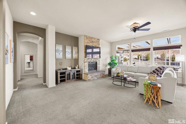 carpeted living room featuring a stone fireplace and ceiling fan