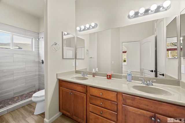 bathroom with hardwood / wood-style flooring, vanity, toilet, and tiled shower