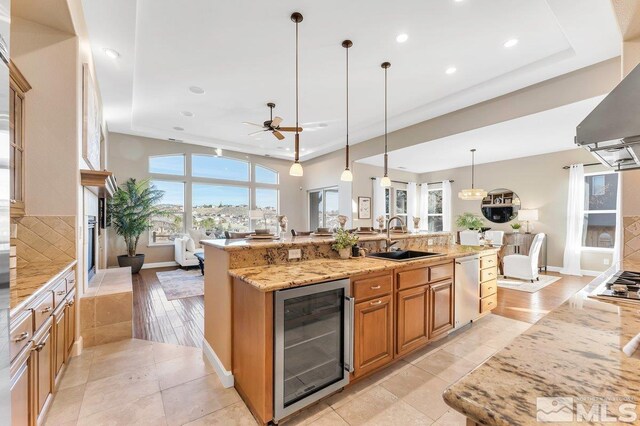 kitchen featuring light stone counters, a large island with sink, light hardwood / wood-style flooring, wine cooler, and hanging light fixtures