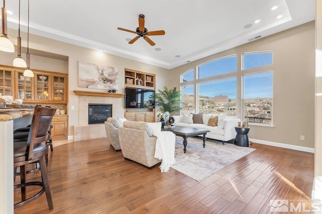 living room featuring a tile fireplace, ceiling fan, built in shelves, and wood-type flooring