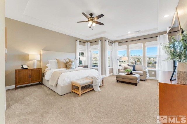 carpeted bedroom with a raised ceiling and ceiling fan