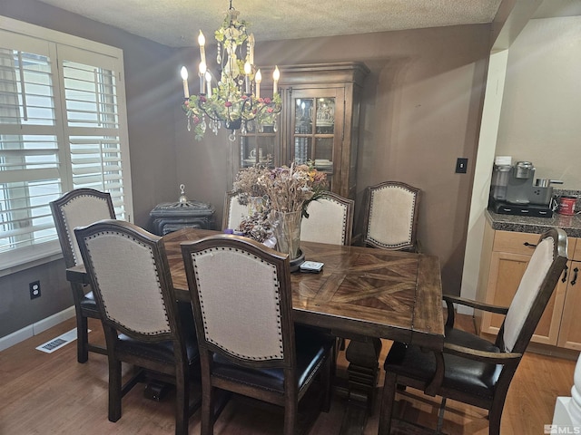 dining area with a chandelier, wood-type flooring, and a textured ceiling