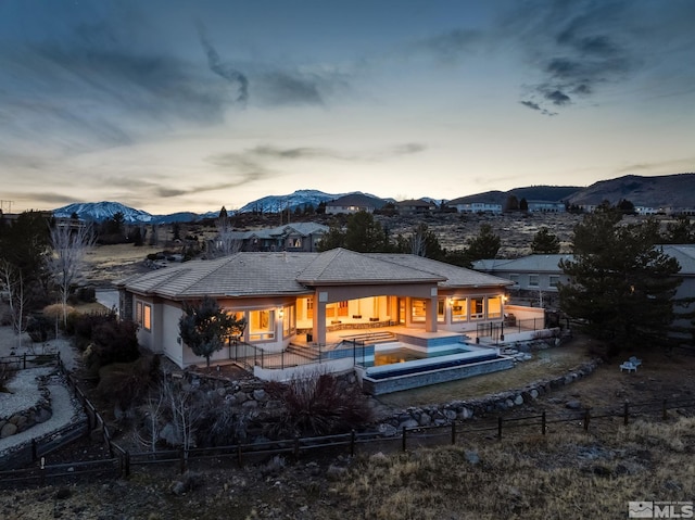 back house at dusk with a mountain view, a patio area, and a pool with hot tub