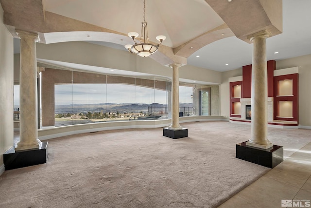 unfurnished living room featuring a notable chandelier, a mountain view, carpet, and decorative columns