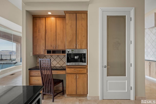 kitchen with decorative backsplash, light tile patterned floors, built in desk, and oven