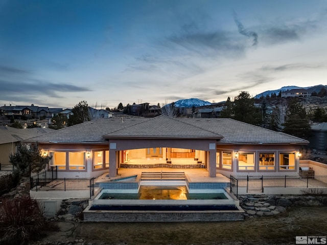 back house at dusk with a mountain view, a swimming pool with hot tub, and a patio area