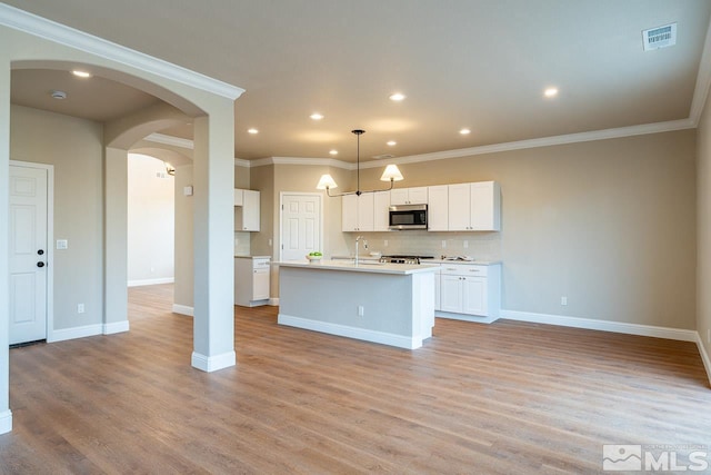 kitchen with stainless steel appliances, pendant lighting, light hardwood / wood-style flooring, white cabinetry, and an island with sink