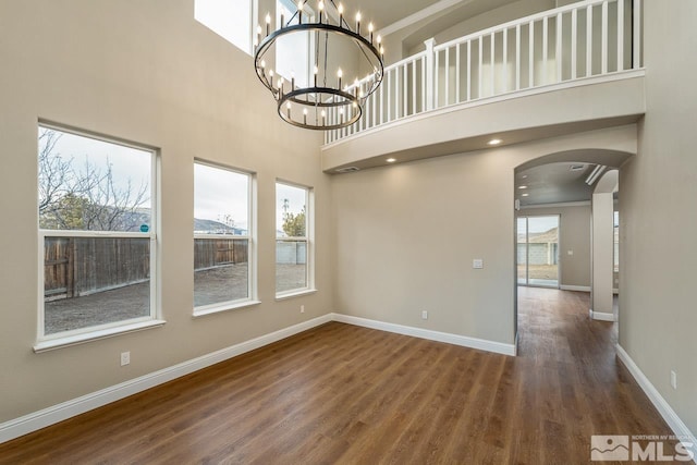 spare room featuring a chandelier, dark wood-type flooring, a towering ceiling, and a healthy amount of sunlight