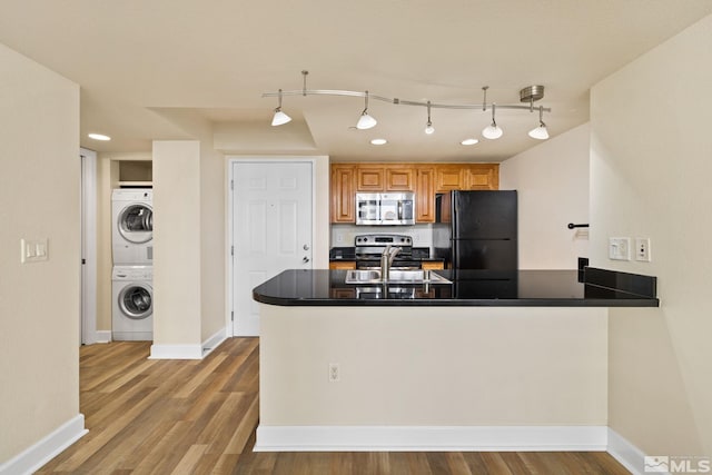 kitchen with kitchen peninsula, black fridge, stacked washer / drying machine, and sink