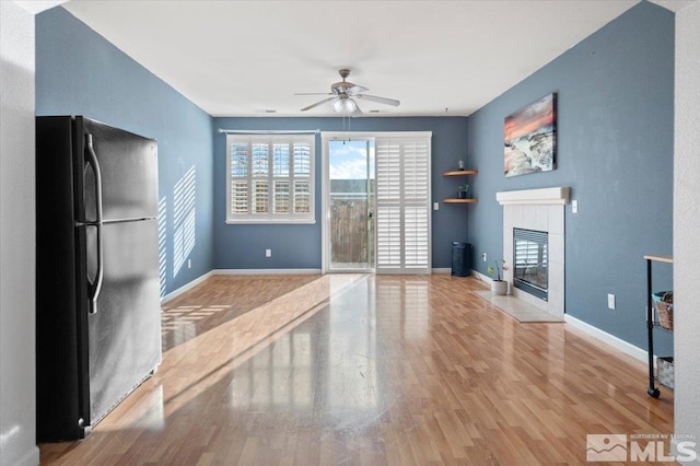 unfurnished living room with a tiled fireplace, ceiling fan, and light hardwood / wood-style floors