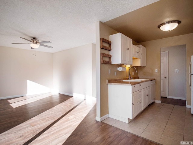 kitchen with white cabinetry, sink, ceiling fan, a textured ceiling, and light wood-type flooring