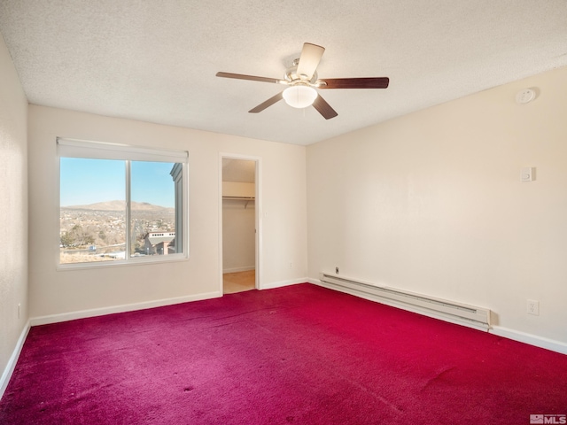 carpeted empty room featuring a mountain view, a textured ceiling, a baseboard radiator, and ceiling fan