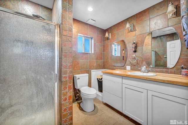 bathroom with vanity, tile walls, tile patterned flooring, toilet, and a shower with shower door