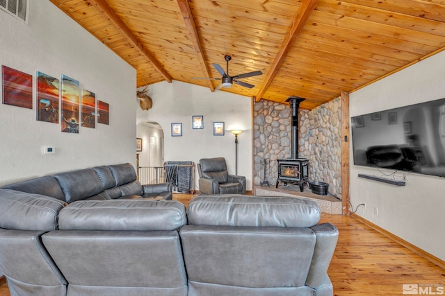 living room featuring a wood stove, vaulted ceiling with beams, ceiling fan, light wood-type flooring, and wood ceiling