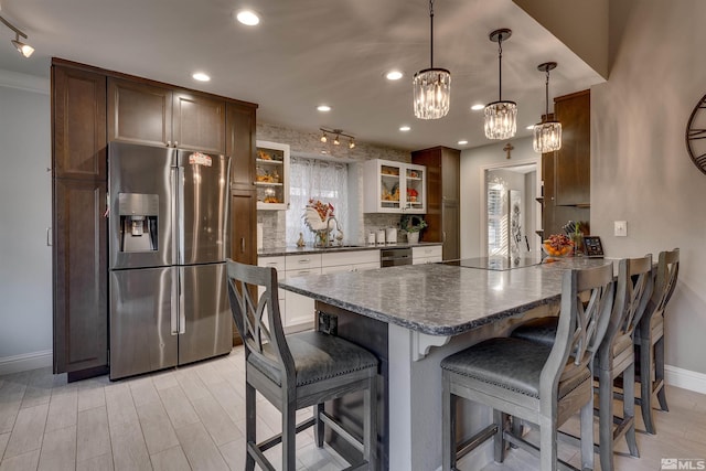 kitchen featuring decorative backsplash, a breakfast bar, stainless steel appliances, white cabinets, and hanging light fixtures