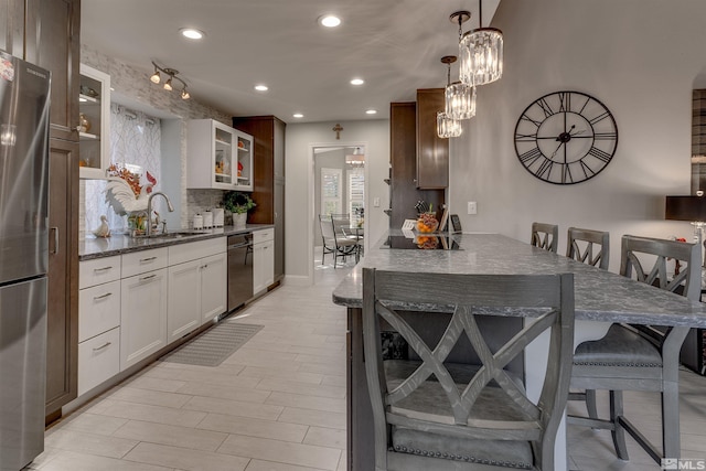 kitchen featuring white cabinetry, sink, stainless steel appliances, decorative light fixtures, and a breakfast bar area