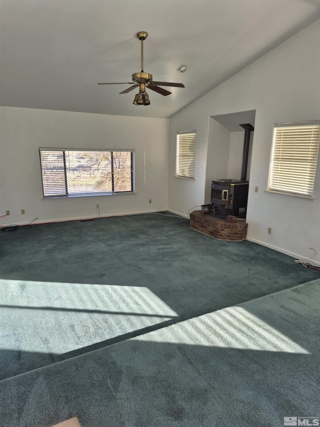 unfurnished living room with a wood stove, ceiling fan, vaulted ceiling, and dark colored carpet