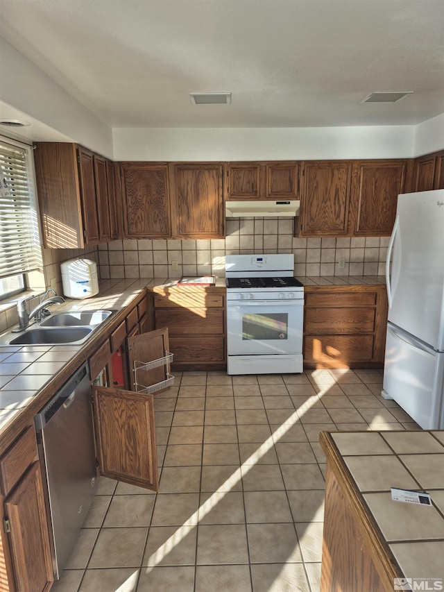 kitchen featuring tile countertops, white appliances, backsplash, sink, and light tile patterned floors