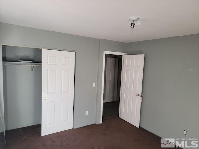 unfurnished bedroom featuring dark carpet and a closet