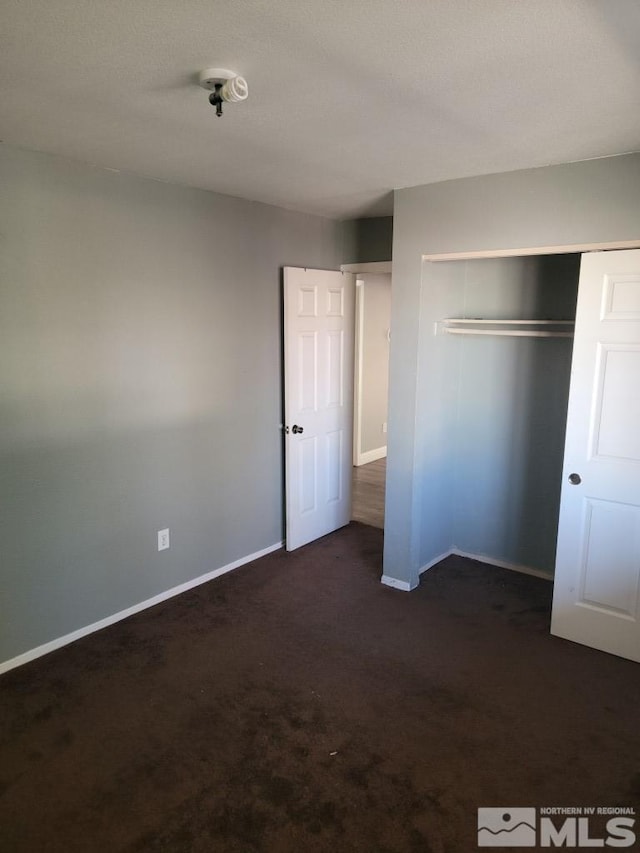 unfurnished bedroom with dark colored carpet and a closet