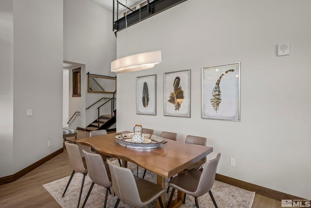 dining space featuring light wood-type flooring and a towering ceiling