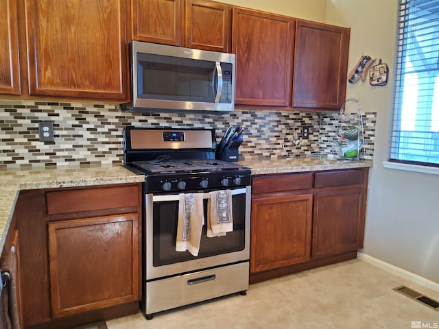 kitchen featuring a healthy amount of sunlight, light stone countertops, appliances with stainless steel finishes, and tasteful backsplash