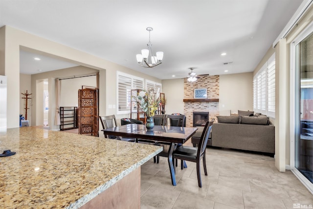 dining space with a stone fireplace, light tile patterned flooring, and ceiling fan with notable chandelier