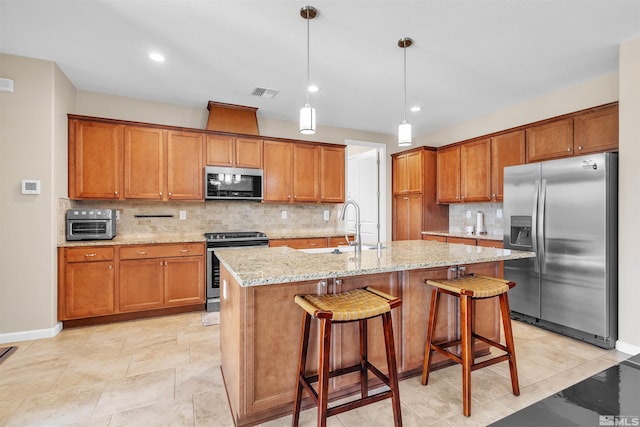 kitchen with pendant lighting, a center island with sink, sink, decorative backsplash, and stainless steel appliances