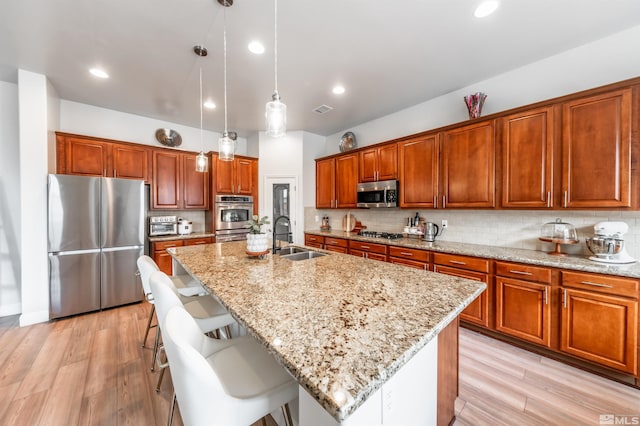 kitchen with a center island with sink, sink, light hardwood / wood-style flooring, decorative light fixtures, and stainless steel appliances