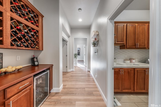 bar featuring decorative backsplash, light hardwood / wood-style floors, light stone counters, and beverage cooler