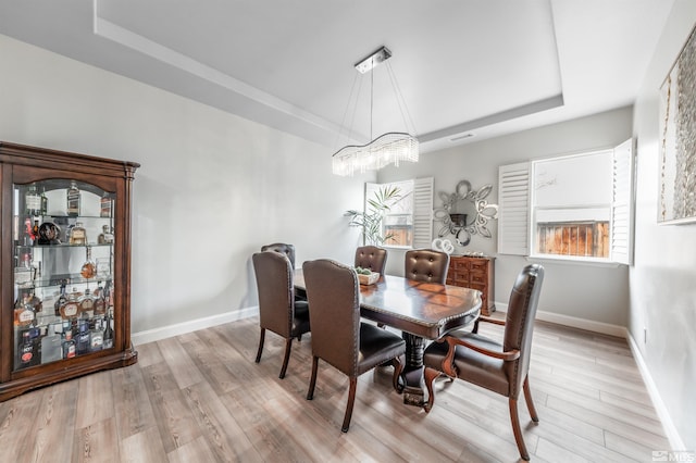 dining space featuring a chandelier, a raised ceiling, and light hardwood / wood-style flooring