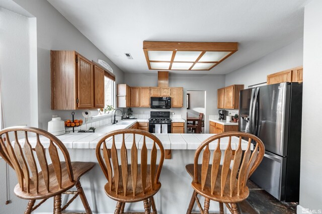 kitchen with tile countertops, black appliances, a peninsula, and a sink