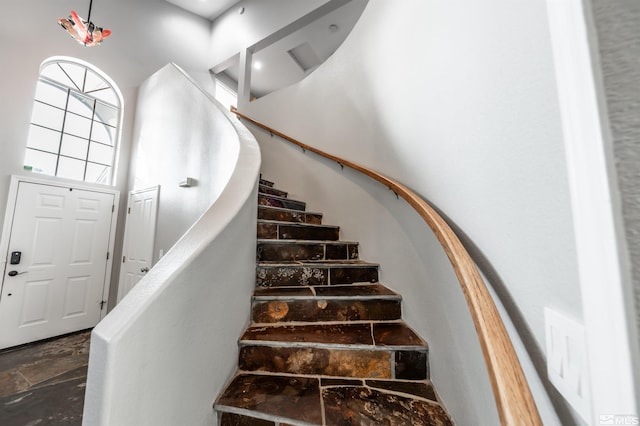 staircase with a towering ceiling and stone tile flooring