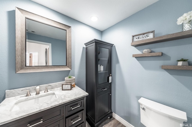 half bath with visible vents, toilet, vanity, wood finished floors, and baseboards