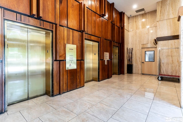 hall with wood walls, light tile patterned floors, a towering ceiling, and elevator