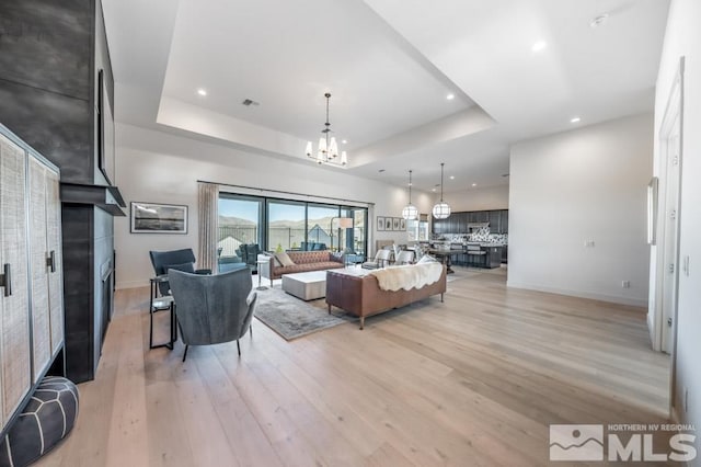 living room with a chandelier, a tray ceiling, and light hardwood / wood-style flooring