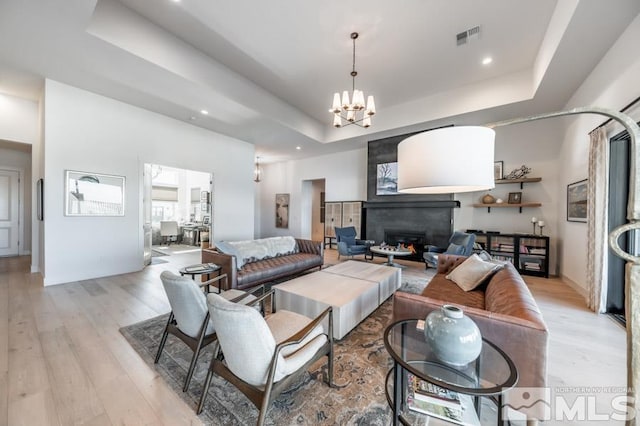 living room with a chandelier, light wood-type flooring, and a tray ceiling