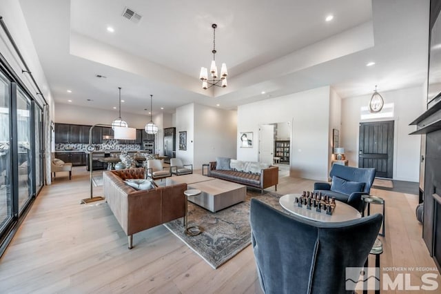 living room with a tray ceiling, light hardwood / wood-style flooring, and a notable chandelier