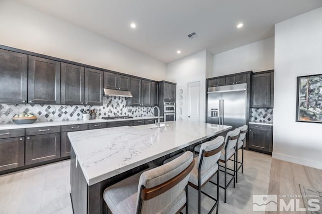 kitchen with appliances with stainless steel finishes, backsplash, and a center island with sink