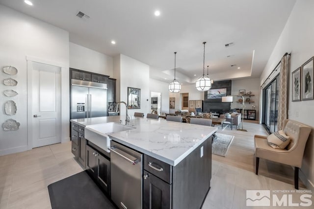 kitchen featuring pendant lighting, sink, light stone countertops, an island with sink, and appliances with stainless steel finishes