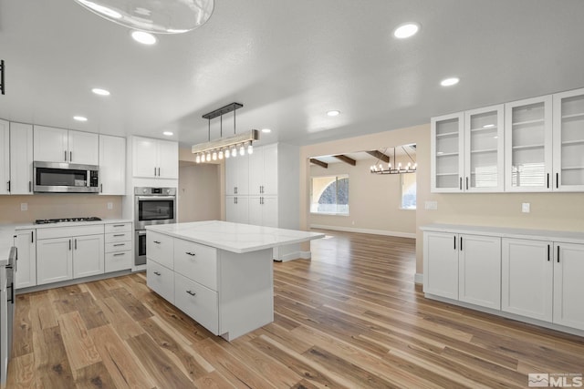 kitchen with white cabinetry, a center island, hanging light fixtures, stainless steel appliances, and light hardwood / wood-style floors