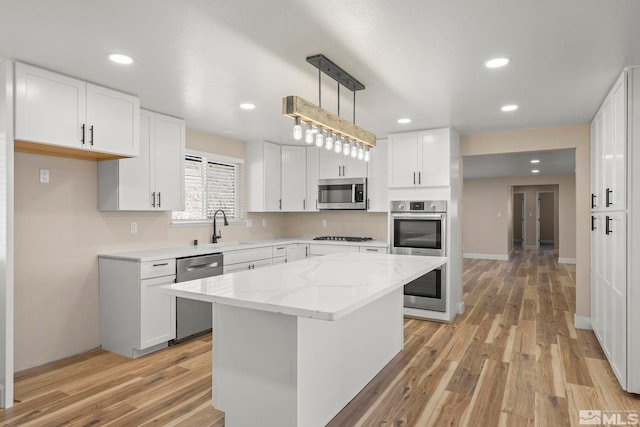 kitchen featuring white cabinets, hanging light fixtures, light hardwood / wood-style floors, appliances with stainless steel finishes, and a kitchen island