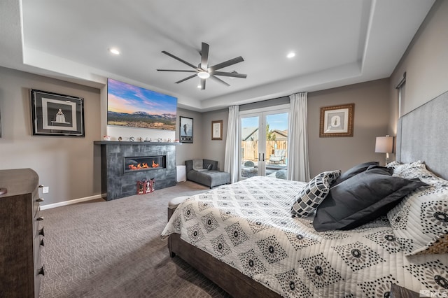 bedroom featuring carpet flooring, a tile fireplace, ceiling fan, a raised ceiling, and access to outside