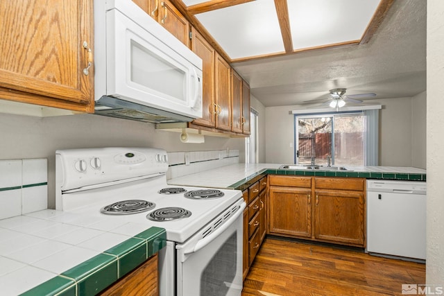 kitchen featuring dark hardwood / wood-style flooring, white appliances, ceiling fan, sink, and tile countertops