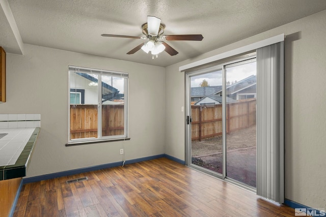 unfurnished dining area featuring a textured ceiling, ceiling fan, and dark wood-type flooring