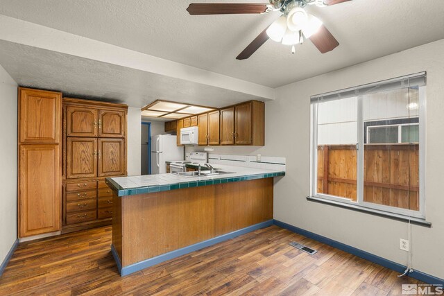 kitchen featuring white appliances, sink, dark hardwood / wood-style floors, tile counters, and kitchen peninsula