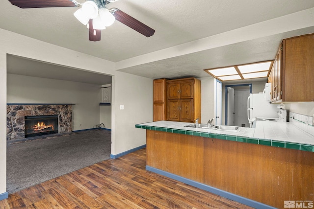 kitchen with kitchen peninsula, tile counters, dark hardwood / wood-style floors, and sink