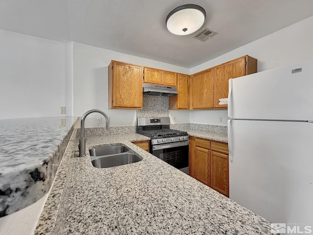 kitchen featuring light stone countertops, tasteful backsplash, stainless steel gas range oven, sink, and white refrigerator