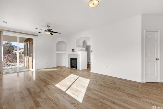 unfurnished living room featuring light wood-type flooring, ceiling fan, and a tiled fireplace