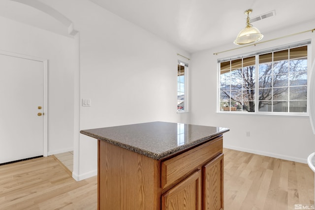 kitchen featuring dark stone countertops, hanging light fixtures, a kitchen island, and light hardwood / wood-style floors